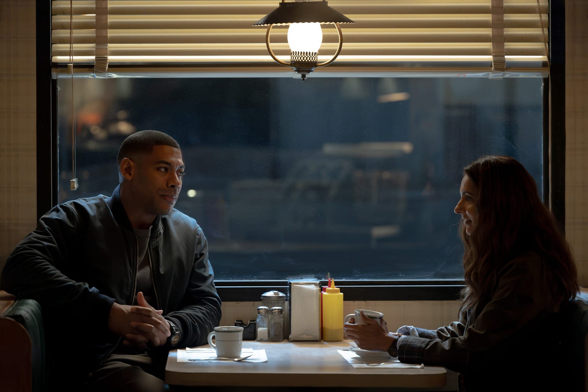 Production still featuring John and Zoe sitting at a booth in a diner.