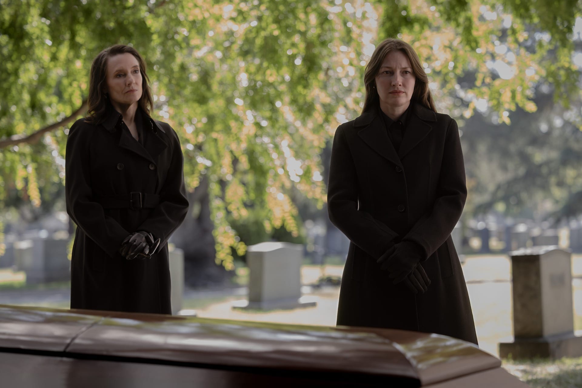 Production still of Carol and Kerry dressed in black coats and standing in a cemetery, standing in front of Hal's casket.
