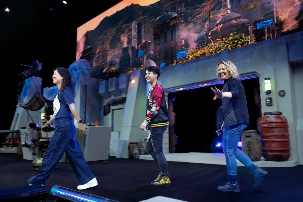 Photograph of three people (Alyssa Wong, Lydia Kang, Tessa Gratton) walking onto a stage with a Star Wars-themed backdrop. All three smile and Tessa waves at the camera.