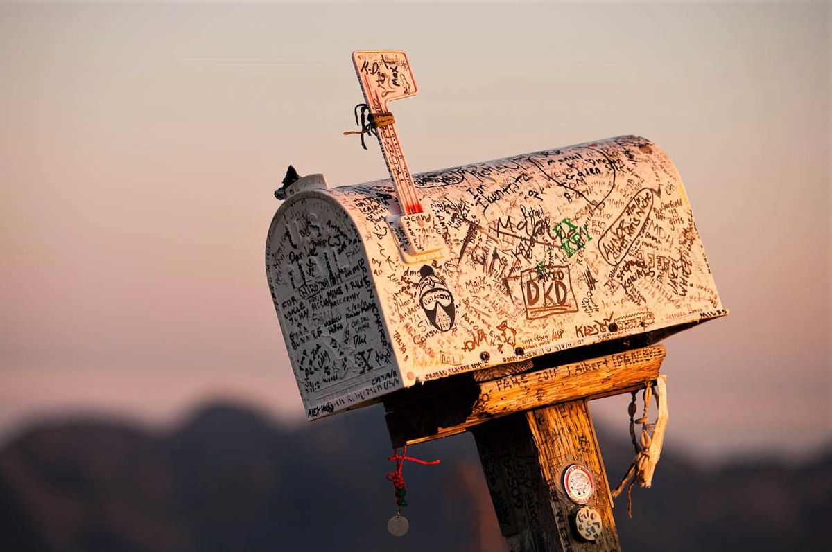 Photograph of a mailbox covered in signatures, cast in the pinkish light of sunset.