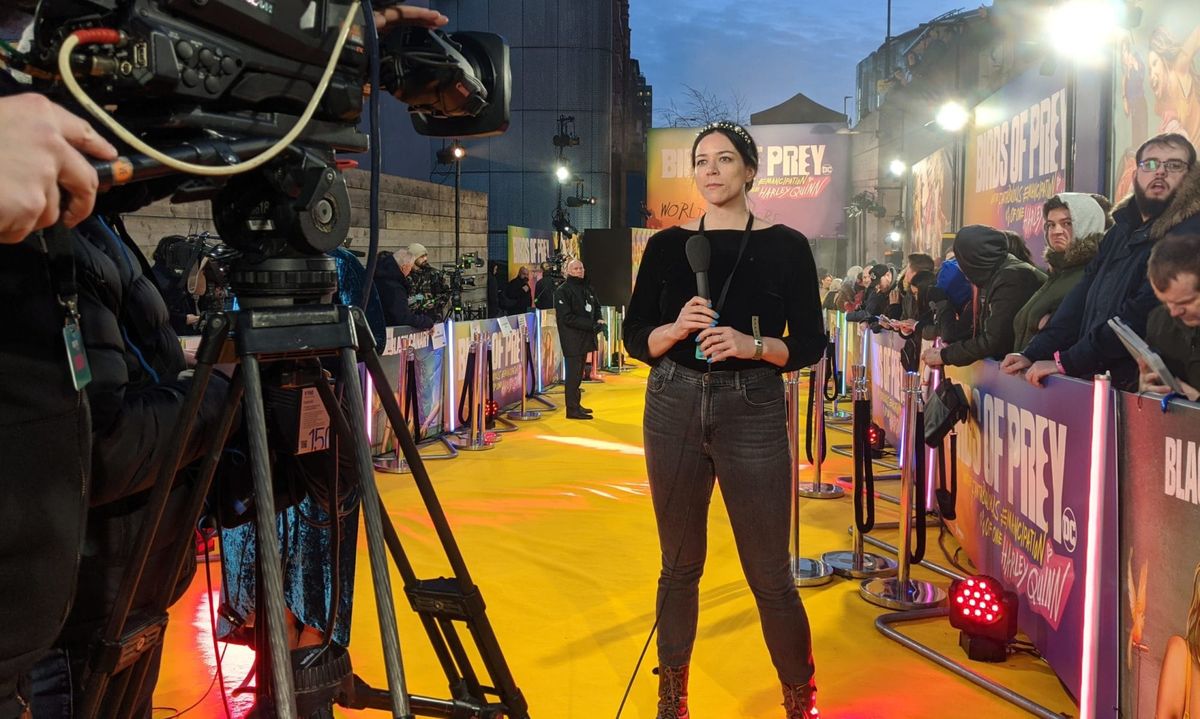 Photograph of Kayti holding a mic and standing in front of a camera at the Birds of Prey film premiere.