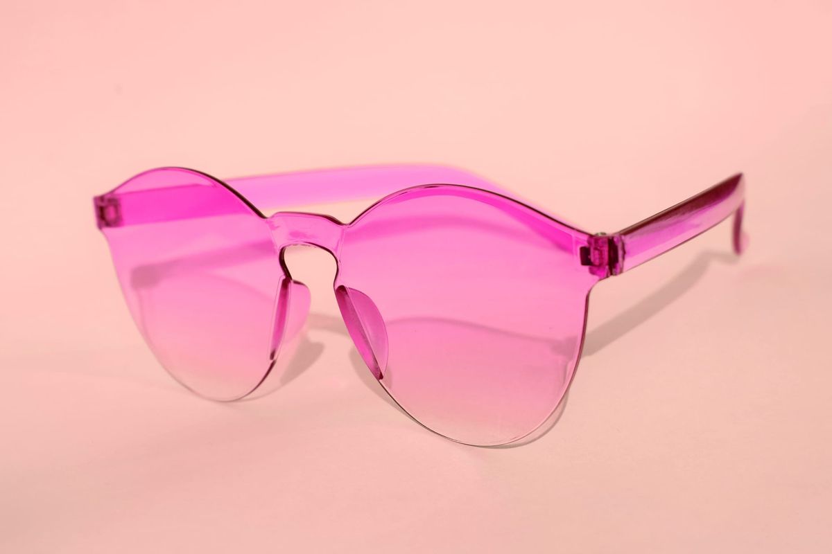 Photograph of a pair of pink-tinted sunglasses against a pink background.