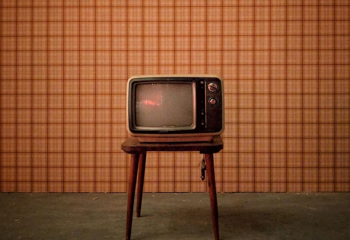 Image of an old television on a small wooden table against a brown and orange checkered wallpaper.