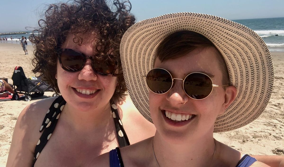 Episode cover: a photograph of Elizabeth and Flourish on Rockaway beach, both wearing bathing suits and sunglasses, Flourish wearing a hat. White fan logo in the corner.