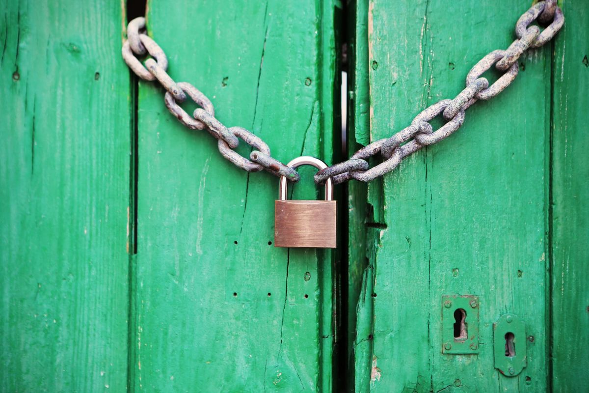 A bright green door shut with a rusty chain and padlock