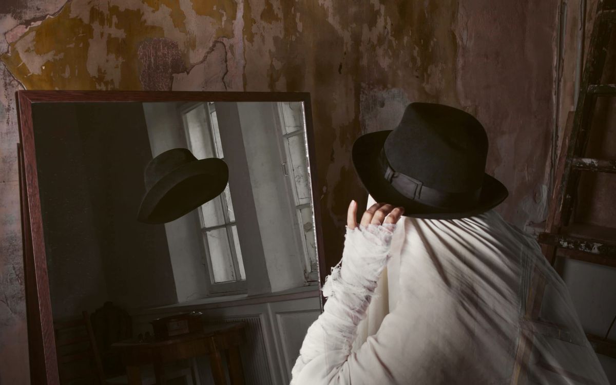 A person in a ghostly costume looking at themselves in a mirror with no reflection.