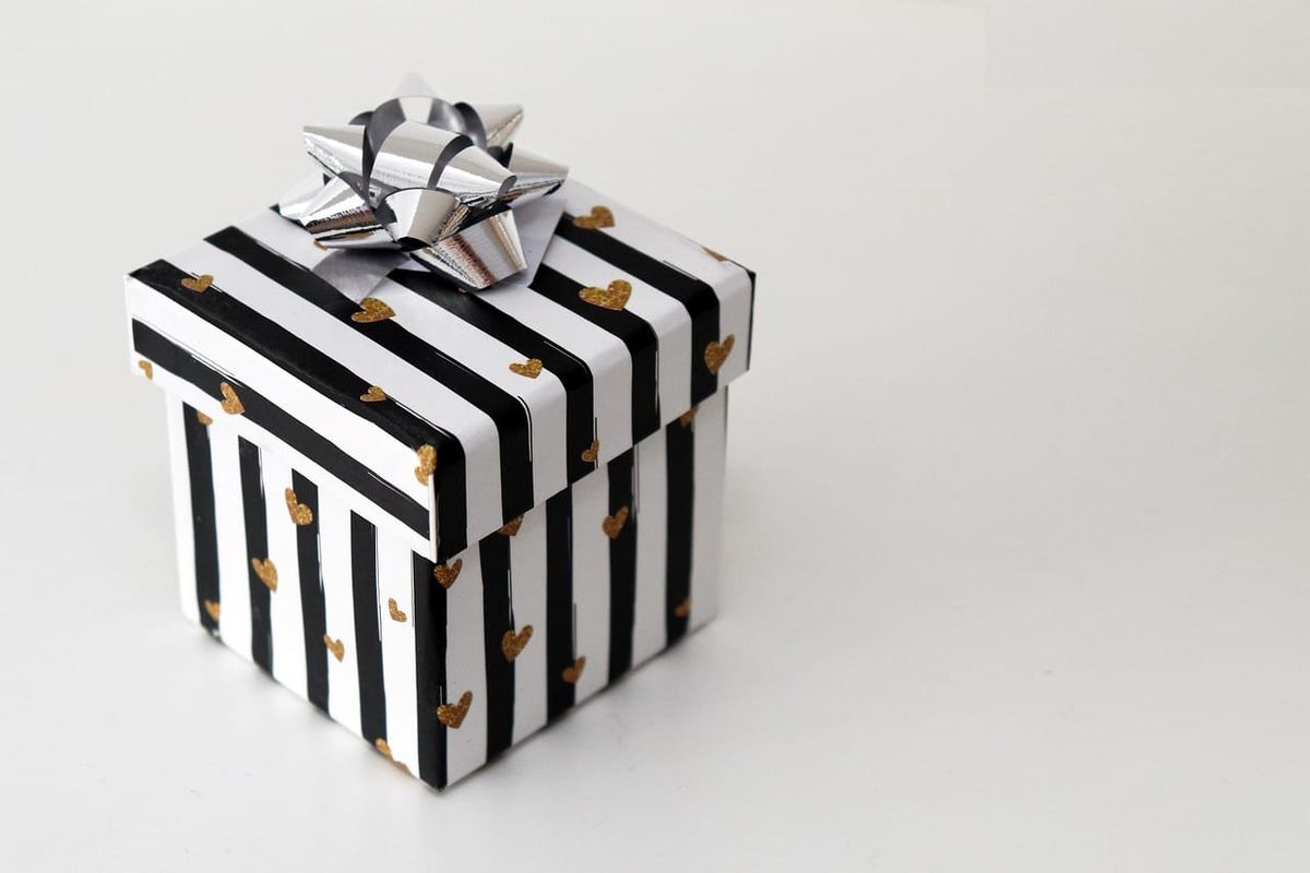 A gift wrapped in paper with black and white stripes and little gold hearts, with a silver bow on top.