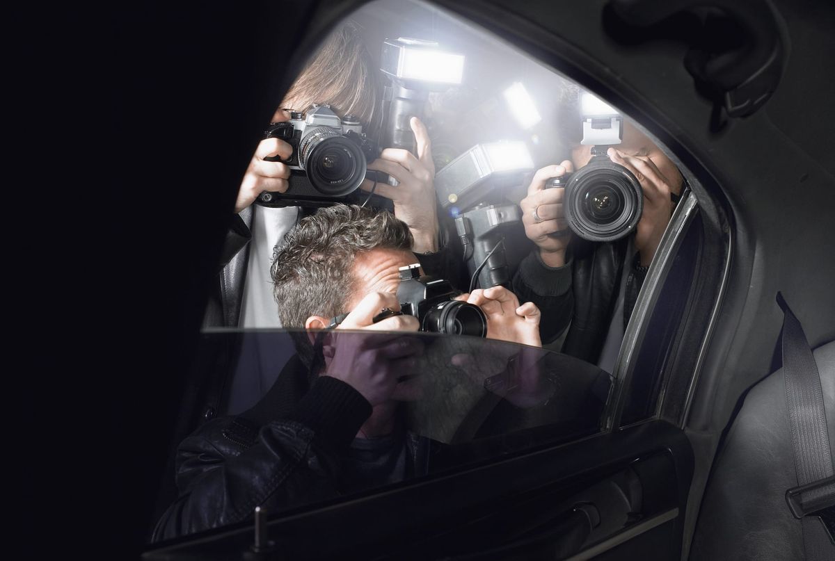 Photograph of several photographers pointing cameras into the backset of a car.