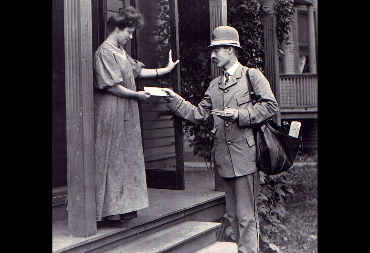 Black and white archival image of a postal worker delivering a letter to its recipient. 