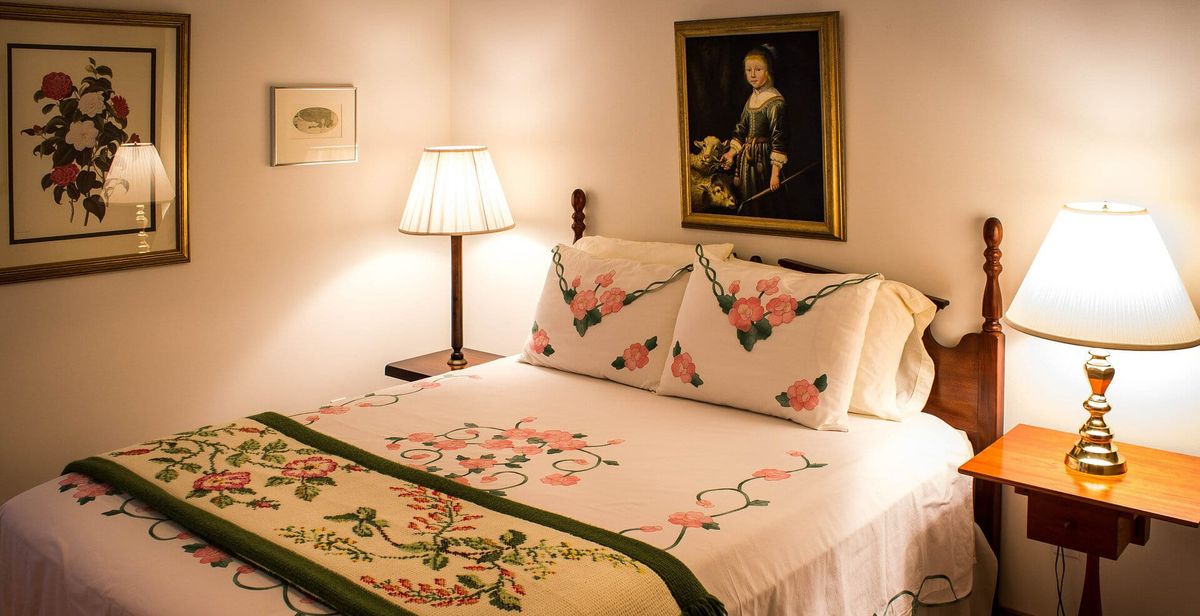A photograph of a bed (much like one might find in a bed and breakfast with only one room left available) with white, green, and pink floral bedding.