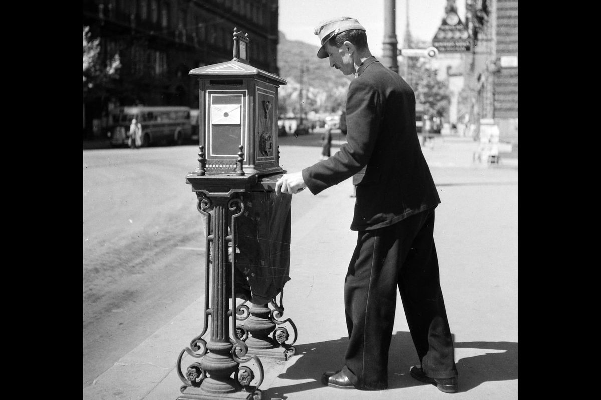 An archival black and white photograph of a postal worker gathering letters. 