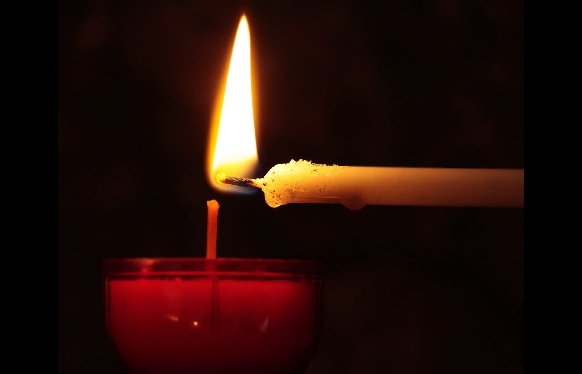 A lit candle is held to an unlit candle at a right angle.
