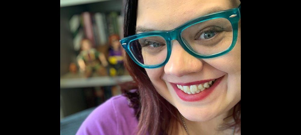 A headshot of Casey Fiesler, wearing fashionable blue glasses.