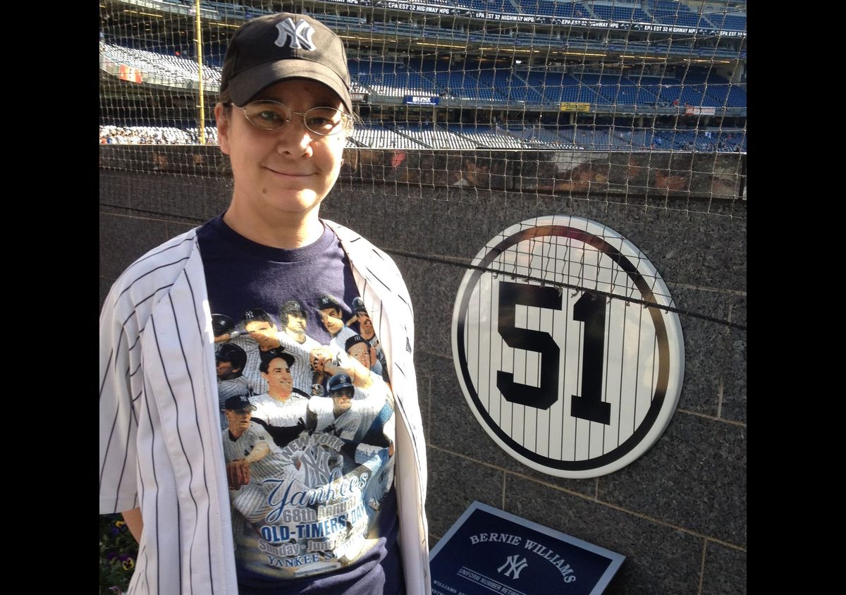 Photograph of Cecilia in Yankees fan gear posing at Yankee Stadium next to a plaque for Bernie Williams