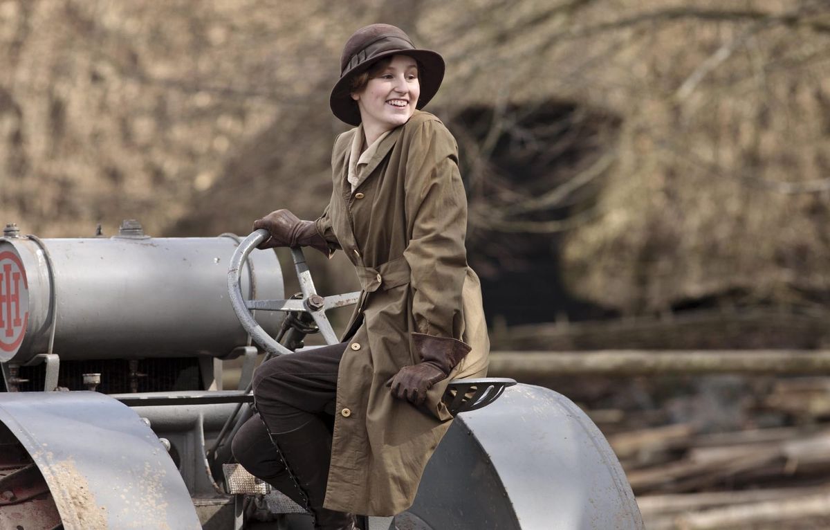 Production still featuring Lady Edith from Downton Abbey driving a sort of old-timey farm vehicle.