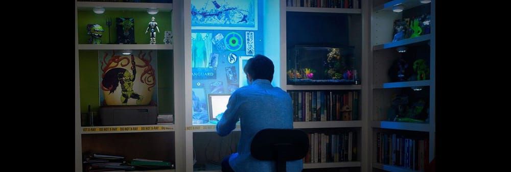 A young man hunches over a computer, late at night. 