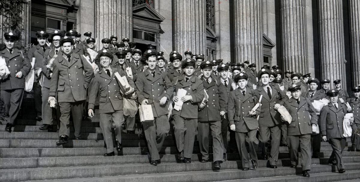 Black and white archival image of a large number of mail carriers walking down a set of grand stairs.