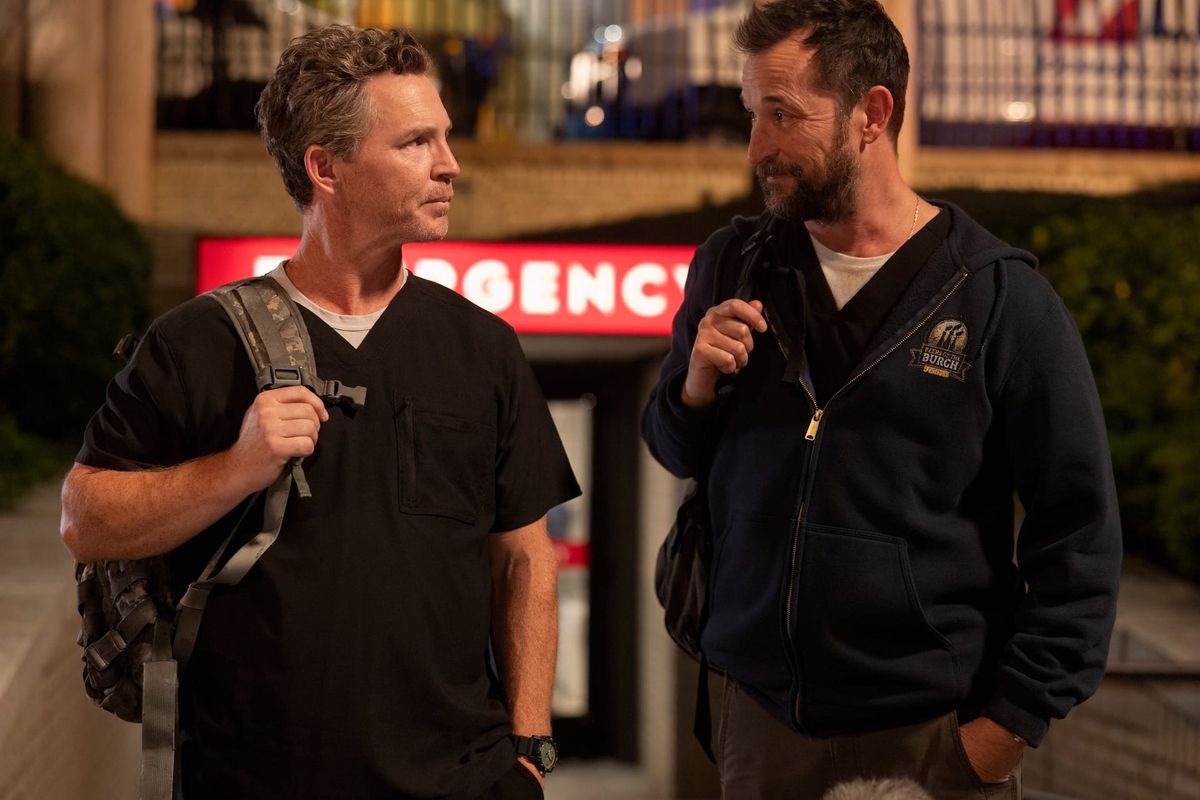 Production still from The Pitt featuring Drs Abbott and Robby standing in front of the red emergency entrance (in the evening), looking meaningfully at each other.