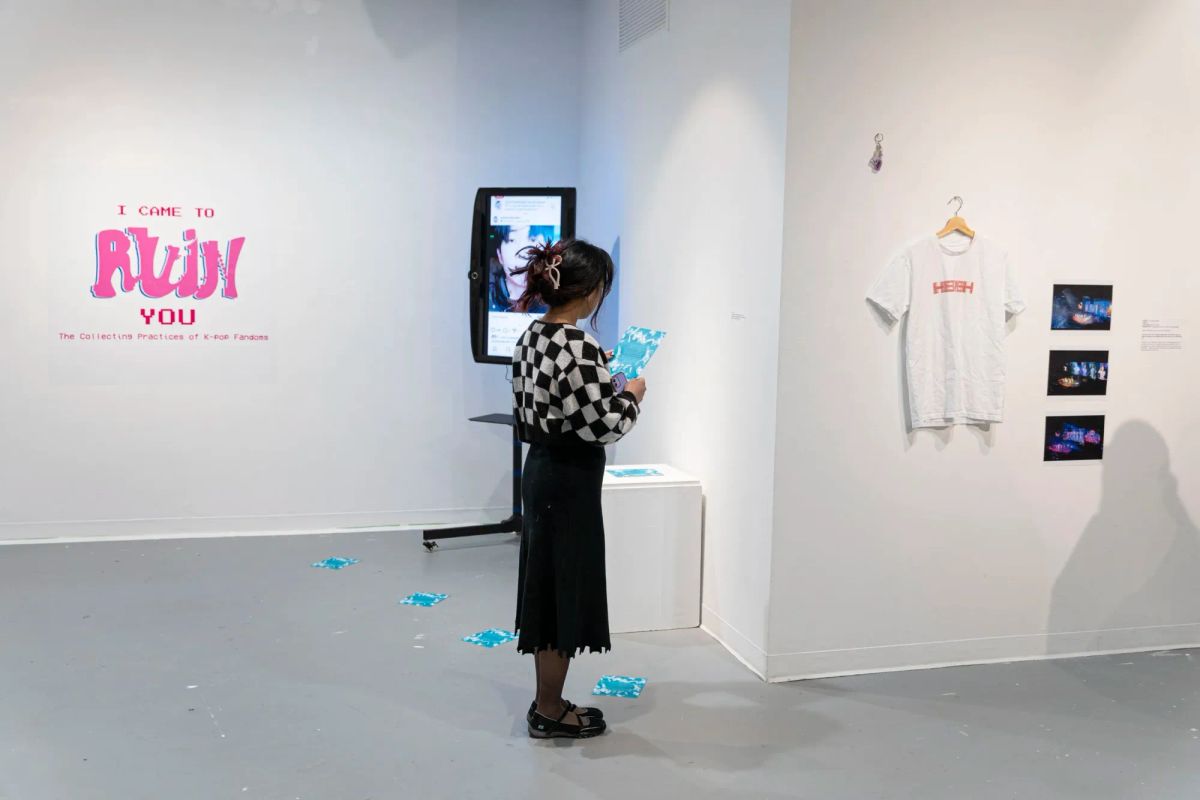 Photo of the exhibition in a white-walled gallery. A figure stands in the center. "I came to RUIN you" on the wall. Video installation in corner. T-shirt hangs in the foreground.