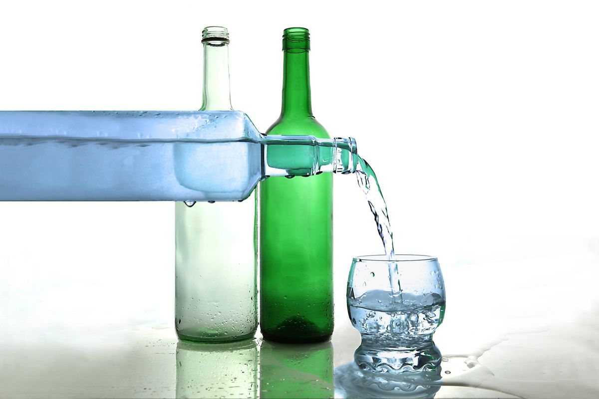 A blue bottle pouring water into a glass, with clear and green bottles sitting behind it.