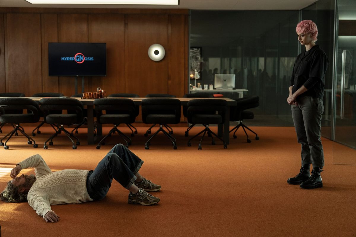 Image of Carl lying on the floor and Harper standing looking down at him. Orange carpet and conference table behind them. TV screen on the wood-paneled wall reads "Hypergnosis".