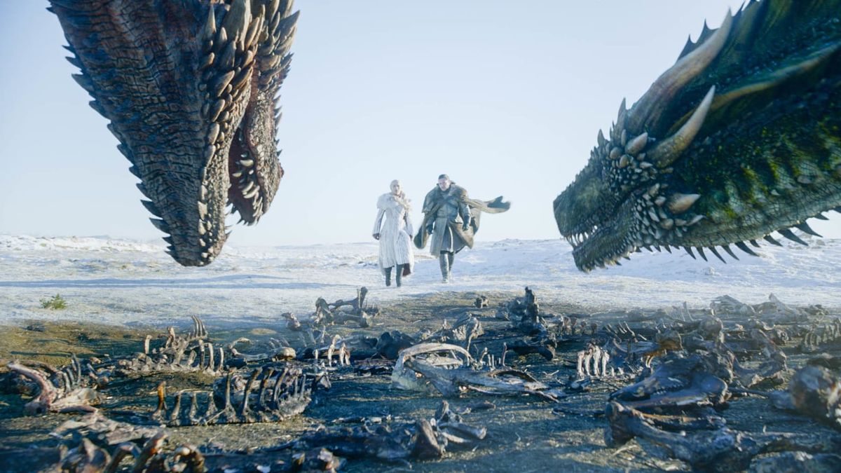 Image from Game of Thrones featuring Daenerys and Jon Snow walking towards a pair of dragons, with many skeletal remains on the ground.