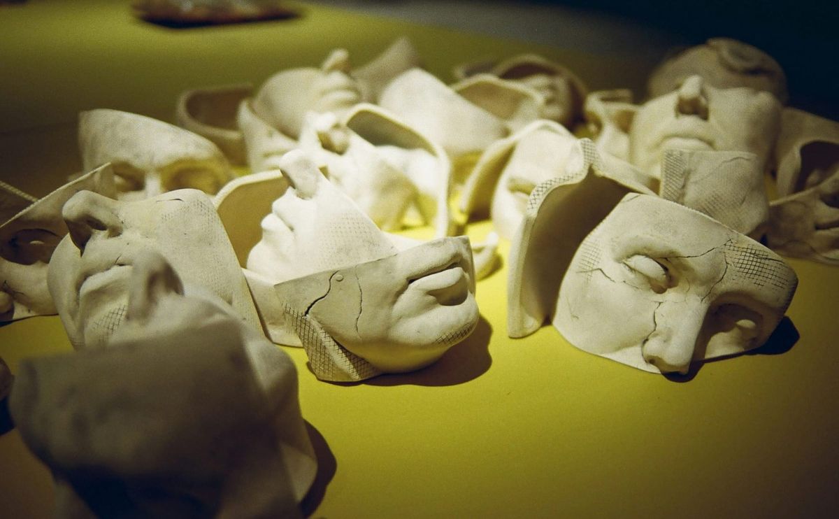 Image of a variety of paster casts of peoples' faces on a yellowish table.