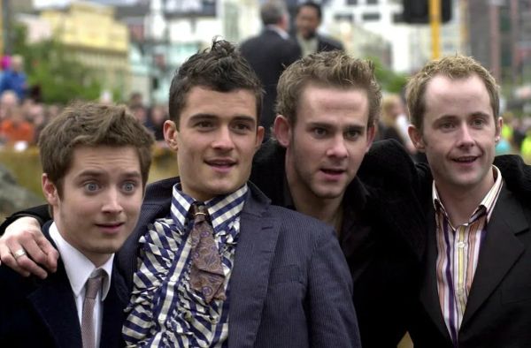 Photograph of actors Elijah Wood, Orlando Bloom, Dominic Monaghan, and Billy Boyd with their arms over each others' shoulders, posing for a photo.