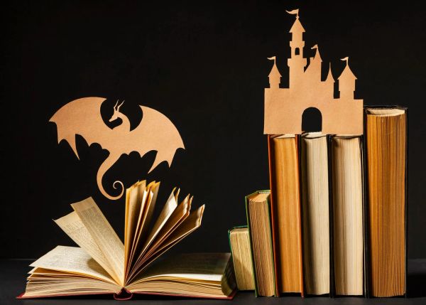 Image of cardboard cut-outs of a dragon and a castle perched atop some books, against a black background. Image via Freepik.