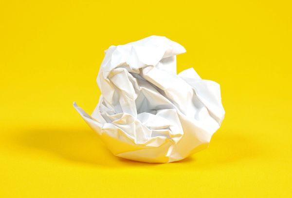 A balled-up sheet of white paper against a bright yellow background.