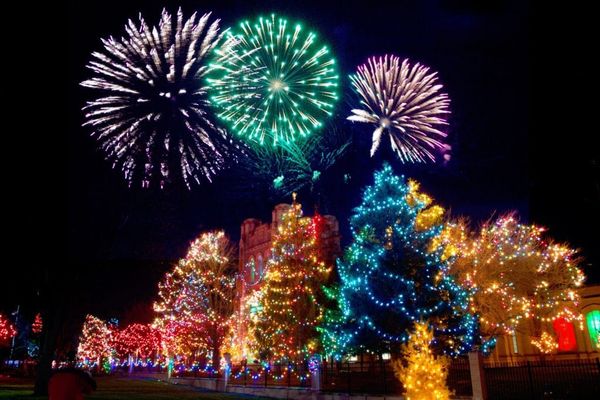 An image of fireworks over a set of buildings decorated in colorful Christmas lights.