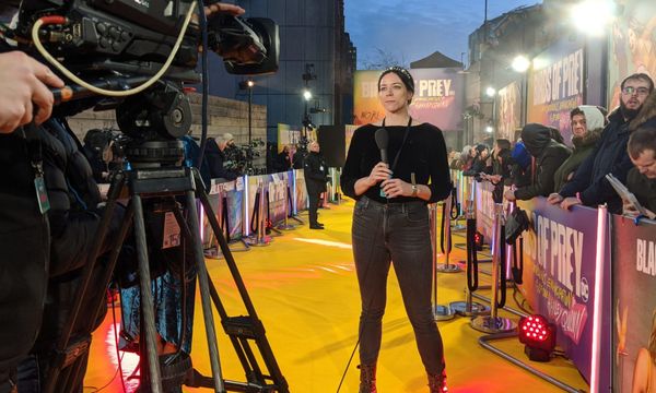 Photograph of Kayti holding a mic and standing in front of a camera at the Birds of Prey film premiere.