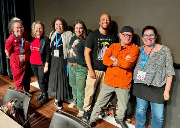 Photograph of the panelists standing on the stage: Meghan, Tessa, Elizabeth, Lin, Brent, Javi, Daphne.