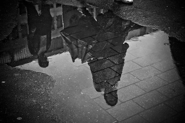 Black and white photograph of two figures' reflections in a puddle.