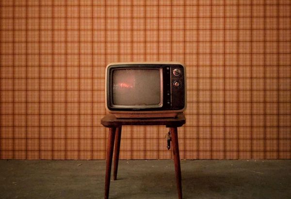 Image of an old television on a small wooden table against a brown and orange checkered wallpaper.