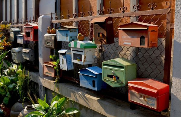 A collection of colorful mailboxes affixed to a chain-link fence.