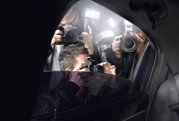 Photograph of several photographers pointing cameras into the backset of a car.
