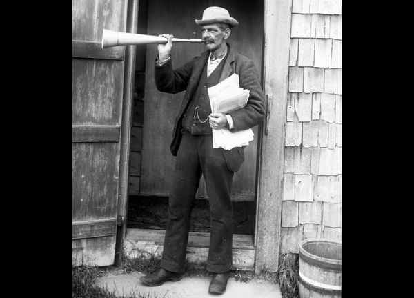 Black and white archival photo of a man with a bullhorn, clutching a sheaf of papers. 
