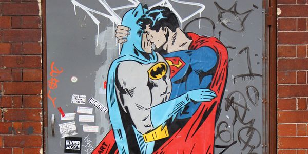 A mural, partially covered in graffiti, of Batman and Superman kissing.