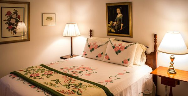 A photograph of a bed (much like one might find in a bed and breakfast with only one room left available) with white, green, and pink floral bedding.