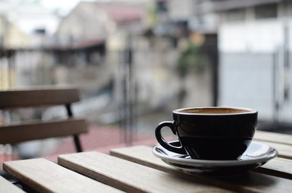 A cup of coffee on a saucer, sitting on an outdoor table.