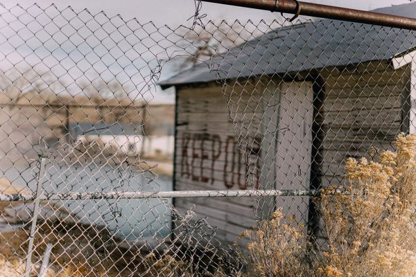 Photograph of a derelict building with a torn fence. Spray painted on the building wall is KEEP OUT. 