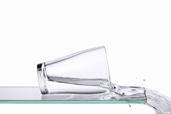 Image of a glass of water spilling over the edge of a glass surface