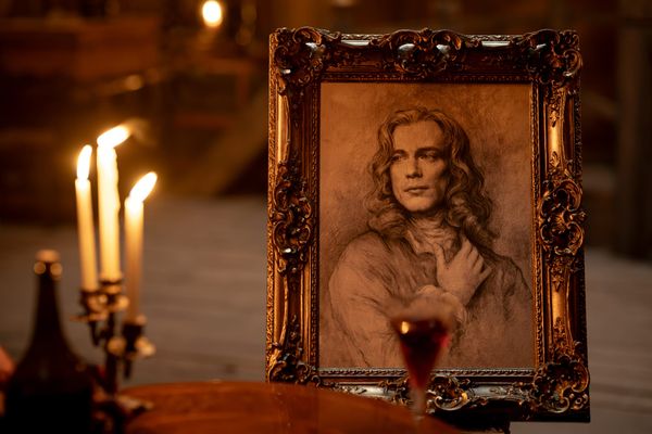 Still from the episode featuring a line drawing of Lestat in a gilded frame, set on a table with a glass of wine and three burning candle