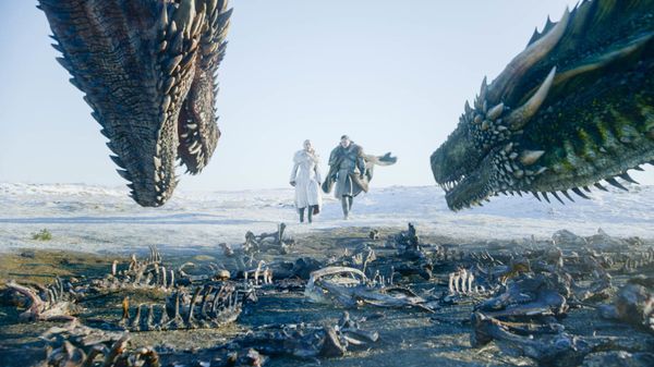 Image from Game of Thrones featuring Daenerys and Jon Snow walking towards a pair of dragons, with many skeletal remains on the ground.