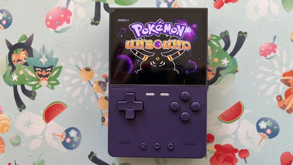 In the center of the image a dark purple gameboy emulator rests flat on an airy light blue Pokémon-patterned fabric, that shows the legendary pokémon Ogerpon in its Teal Mask form.