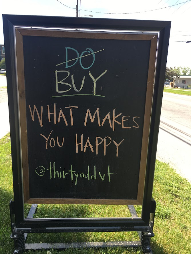 Blackboard on a strip of grass that reads "Do Buy what makes you happy" with the "do"crossed out.