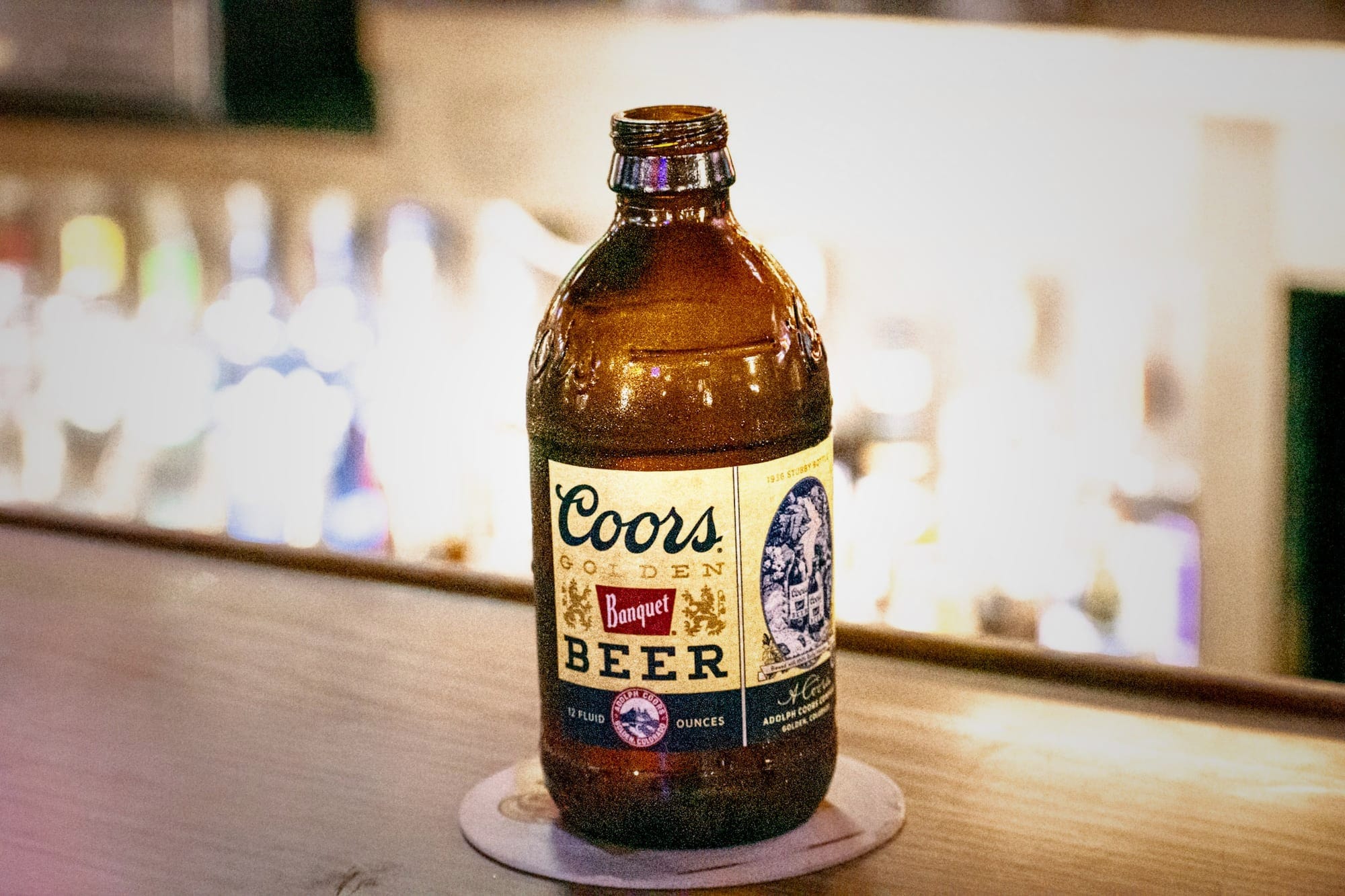 a Coors Banquet bottle beads with condensation on an illuminated plywood bar