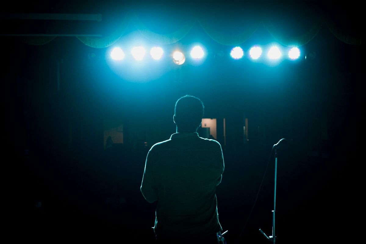 Lonely performer anxiously staring on stage in a dark air room nervous before a performance