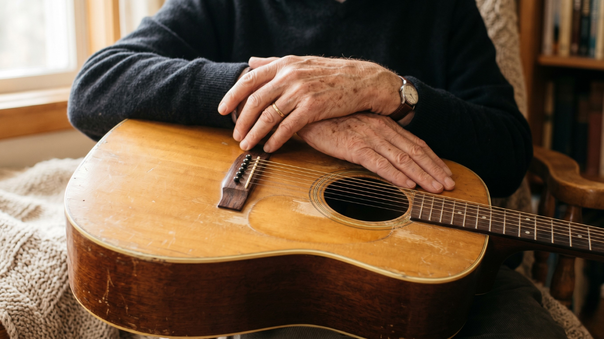 older guitarist's hands resting on acoustic guitar body, soft natural light.